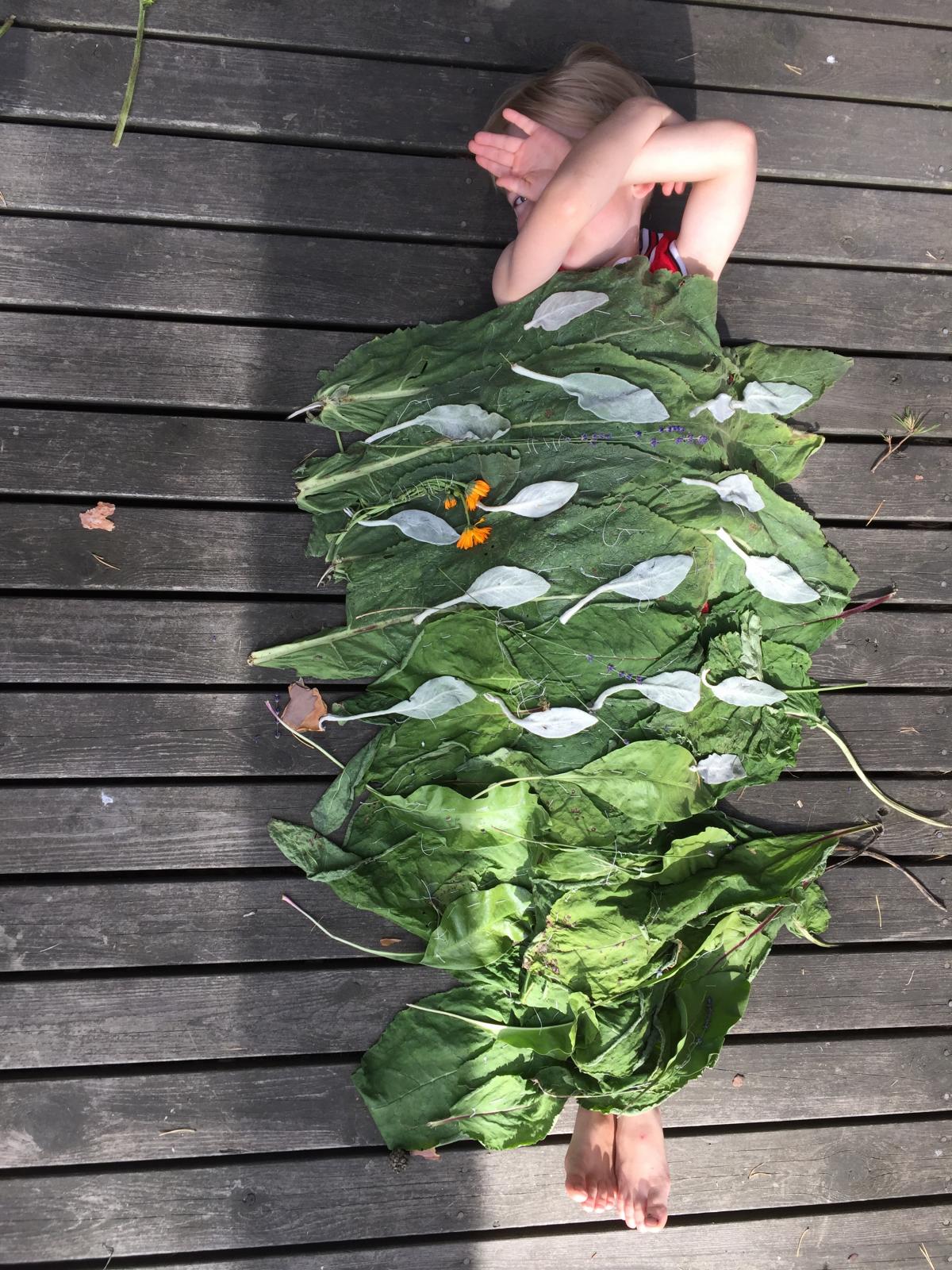 Lapsi makaa lehdistä tehdyn peiton alla.