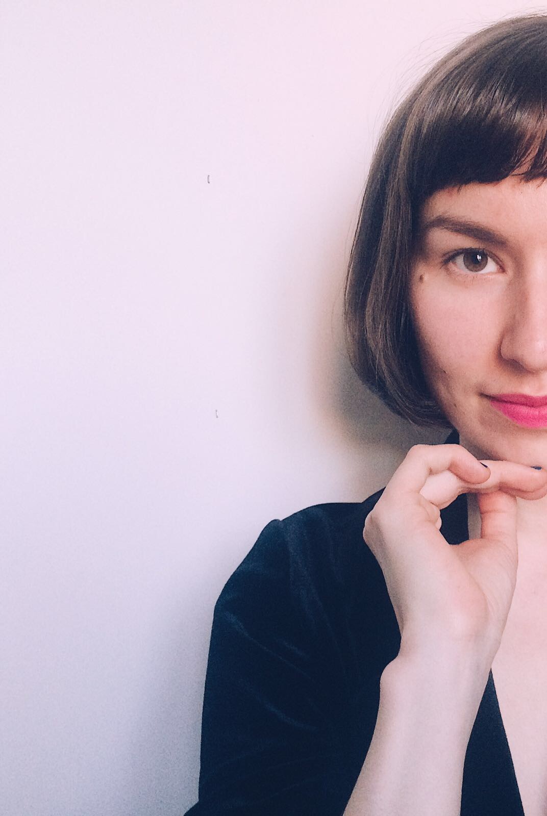 Aino Rautakorpi on kuvassa vaaleanpunaista seinää vasten. Puolet hänen kasvoista on näkyvissä.